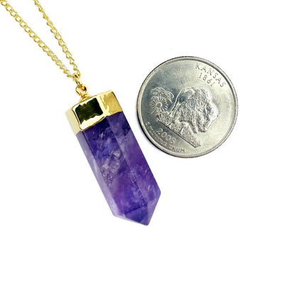 An amethyst point necklace next to a quarter for sizereference