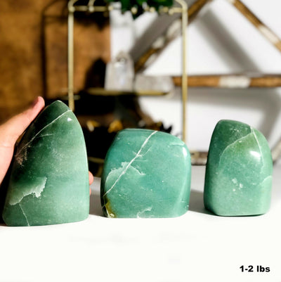 hand holding 1-2lbs aventurine cut base with 2 others with decorations blurred in the background