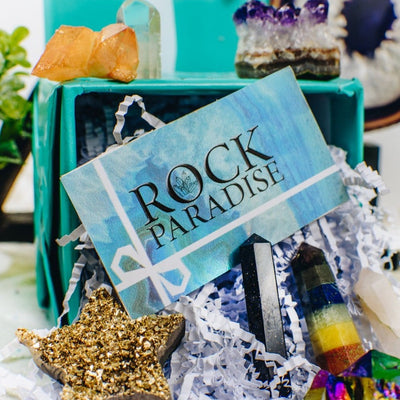 A blue card with Rock Paradise written on it surrounded by assorted crystals.