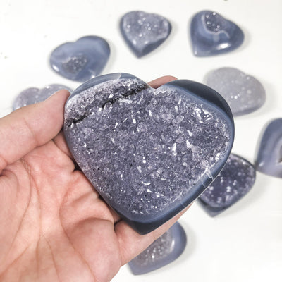 Close up of one agate druzy heart in a hand multiple agate hearts in the background.