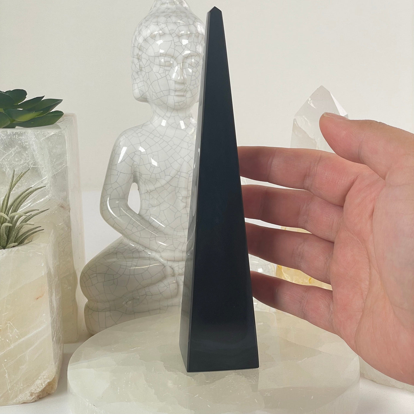 Silver Sheen Obsidian Crystal Obelisk - One-of-a-Kind #2 with hand for size reference with props and plants in the background