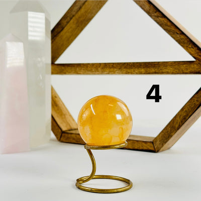 Golden Healer Crystal Sphere labeled variant 4 on a metal stand on a white table with a wood shelf and two crystal points in the background