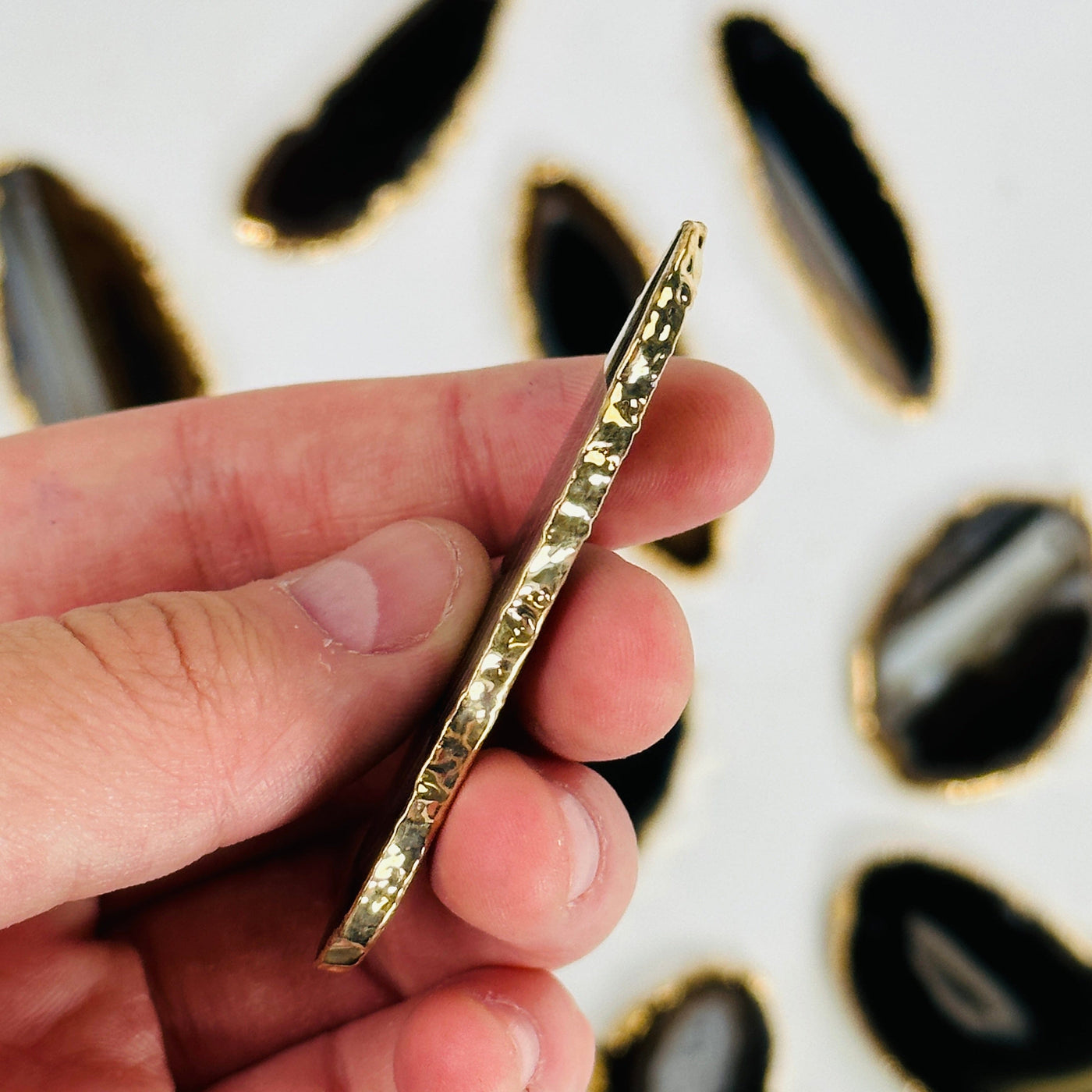 fingers holding up brown agate slice showing gold edge and thickness with others in the background