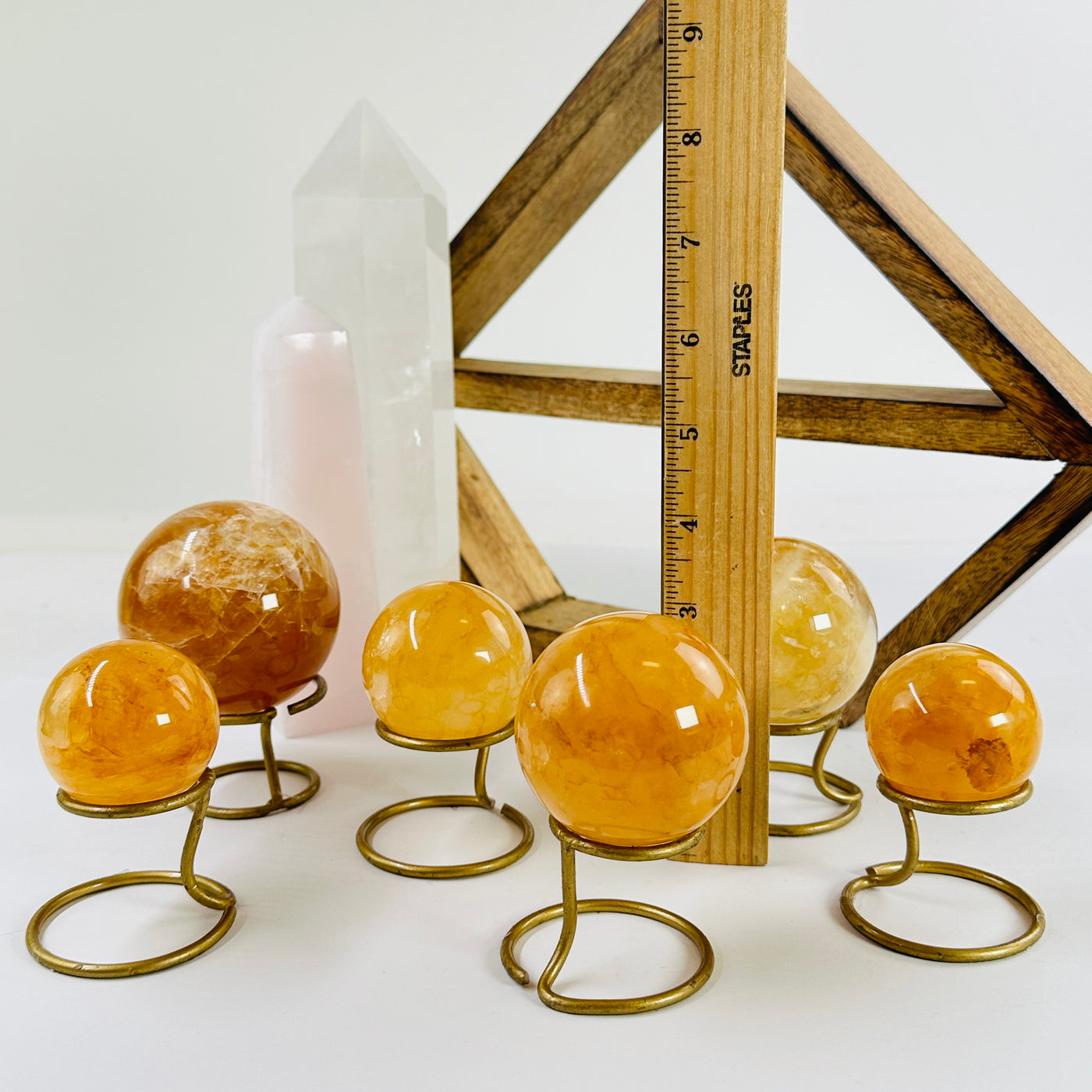 6 Golden Healer Crystal Spheres on metal stands with a ruler for size reference with a wood shelf and 2 crystal points in the background