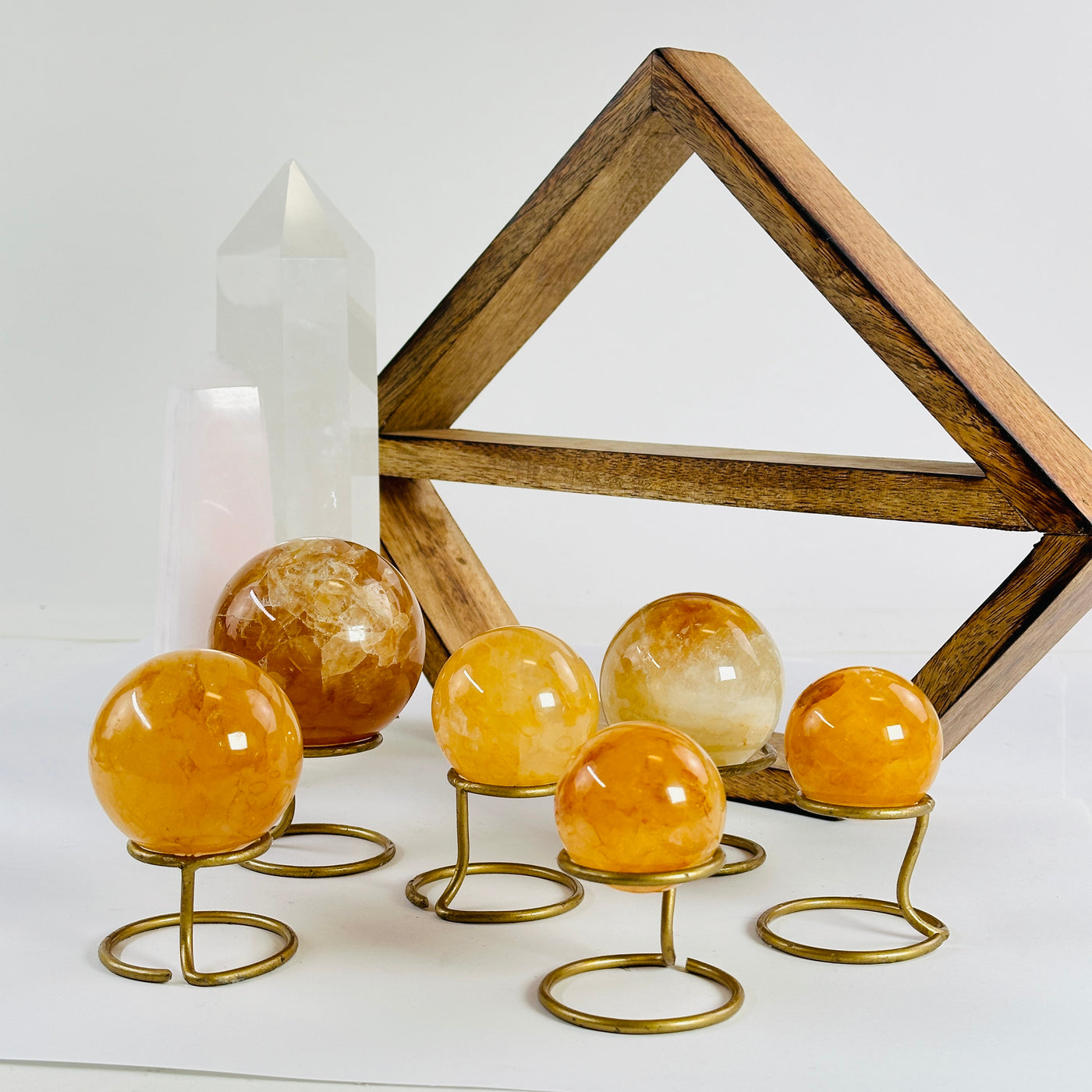  6 Golden Healer Crystal Spheres on metal stands on a white table with a wood shelf and 2 crystal points in the background.