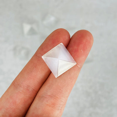 fingers holding up selenite pyramid with others in the background