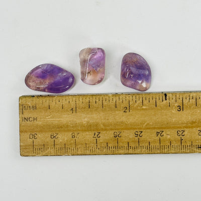 ametrine tumbled stones next to a ruler for size reference