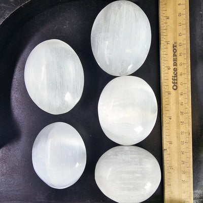 Selenite Crystal Palm Stones 5 palm stones of different sizes next to ruler for size reference