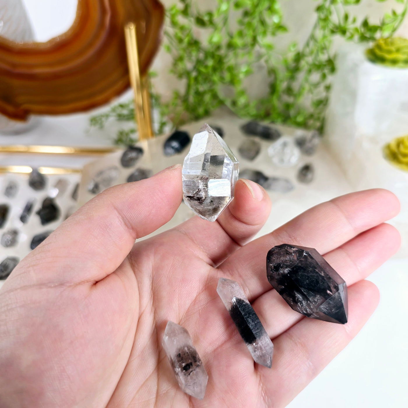 Tibetan Quartz - Double-Terminated Crystal Points - By Size Large variant between thumb and index finger with other size variants in hand and more variants in the background with props