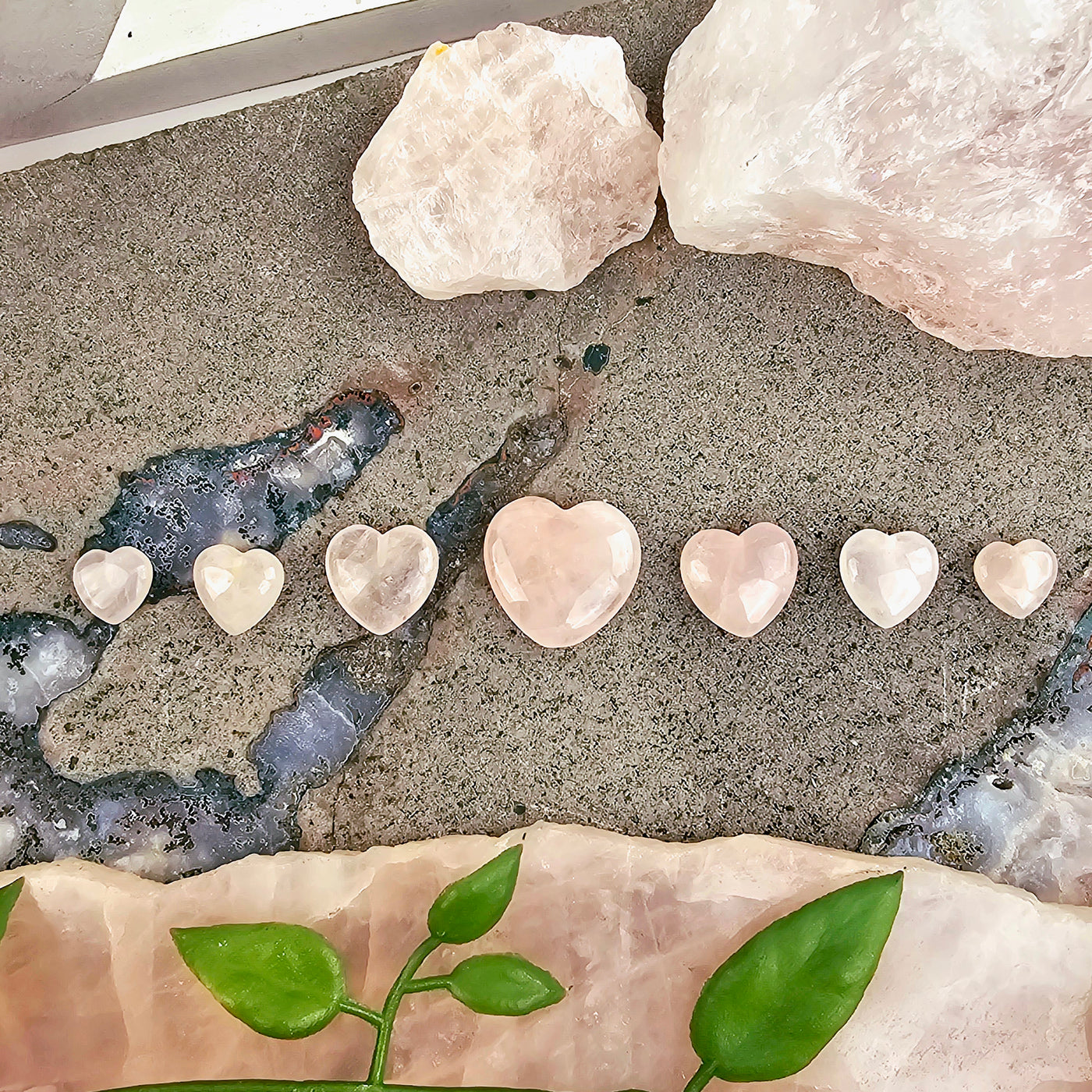 Rose Quartz Crystal Hearts - By Size arranged aesthetically on crystal platter with props and plants in the background