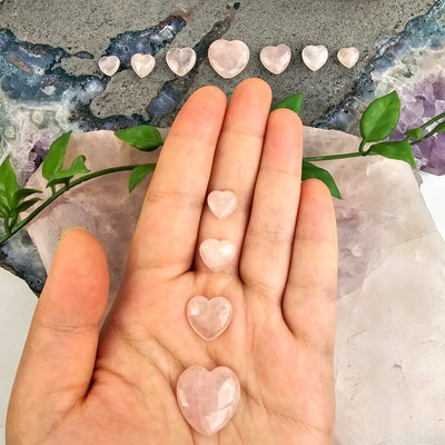 Rose Quartz Crystal Hearts - By Size all variants in hand for size reference with more variants in the background on an amethyst platter