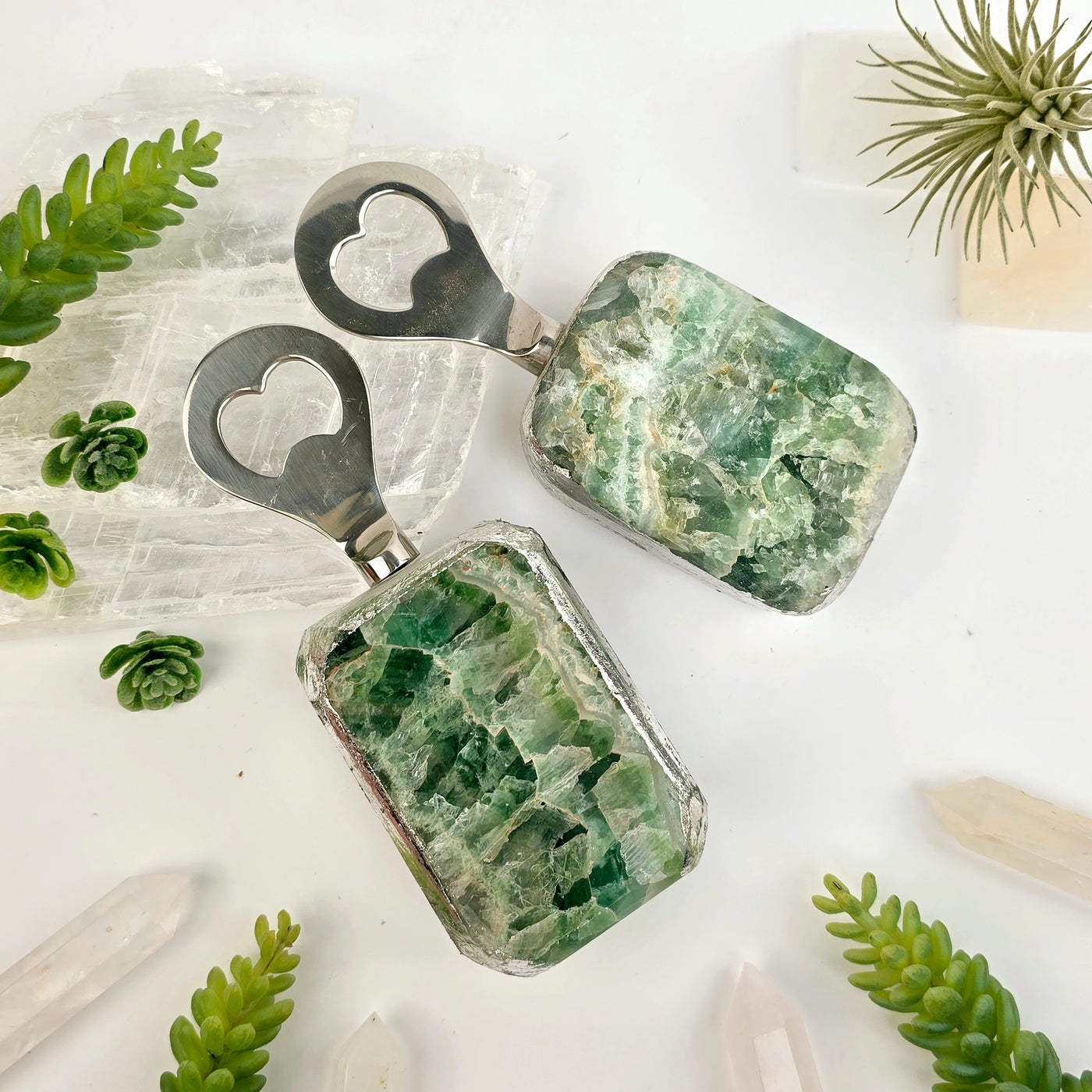 Green Fluorite Bottle Opener - 2 bottle openers, one polished side and one rough side, with props and plants in the background, top view