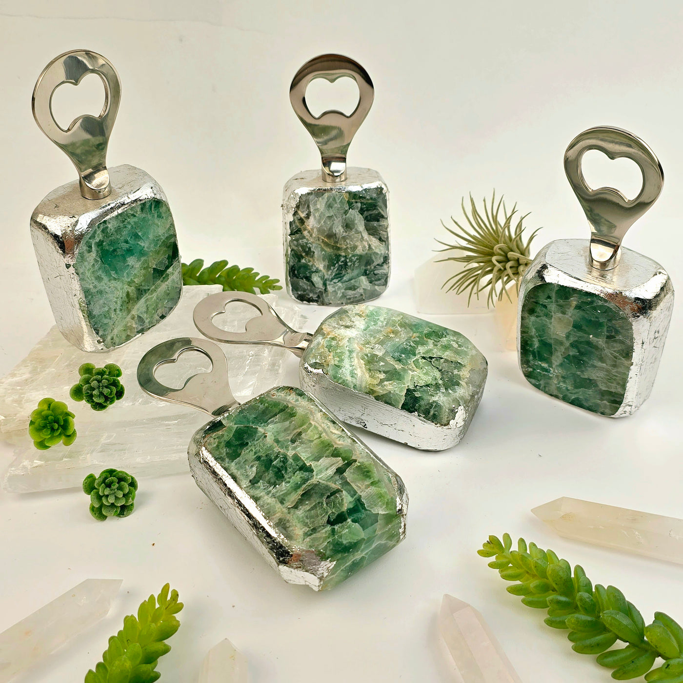 Green Fluorite Bottle Opener 3 bottle openers standing up with two lying propped up on selenite slab with plants in the background