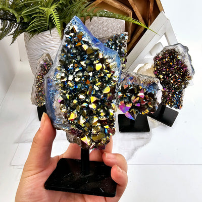 Titanium Coated Amethyst Cluster on Stand - You Choose variant 1 in hand for size reference with other variants in the background with props and plants