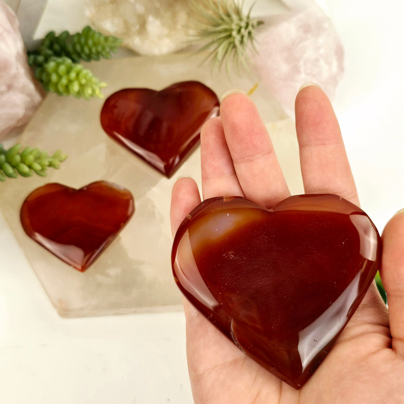 Carnelian Crystal Hearts - You Choose variant C in hand for size reference with other variants in the background