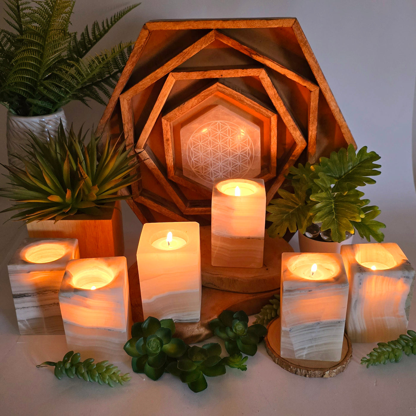 Mexican Onyx Rectangular Crystal Candle Holder candles lit inside in dim light emitting warm glow on props and plants in the background