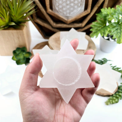 Selenite Six-Pointed Star Candle Holder in hand for size reference with other selenite candle holders in the background