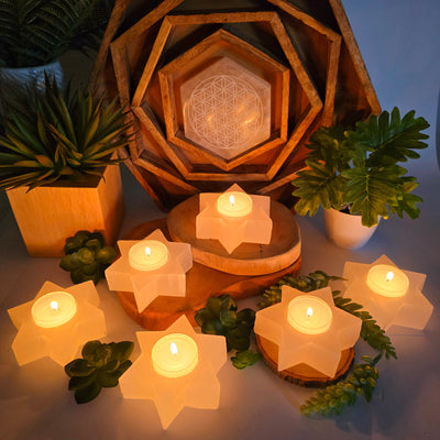 Selenite Six-Pointed Star Candle Holder in dim lighting with candles lit with props and plants in the background