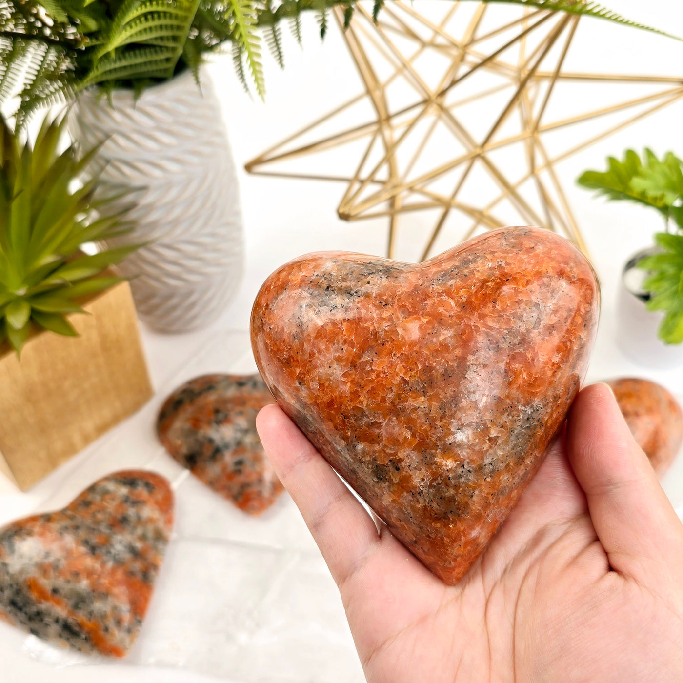 Large Orchid Calcite Polished Heart - By Weight in hand for size reference with other variants with props and plants in the background