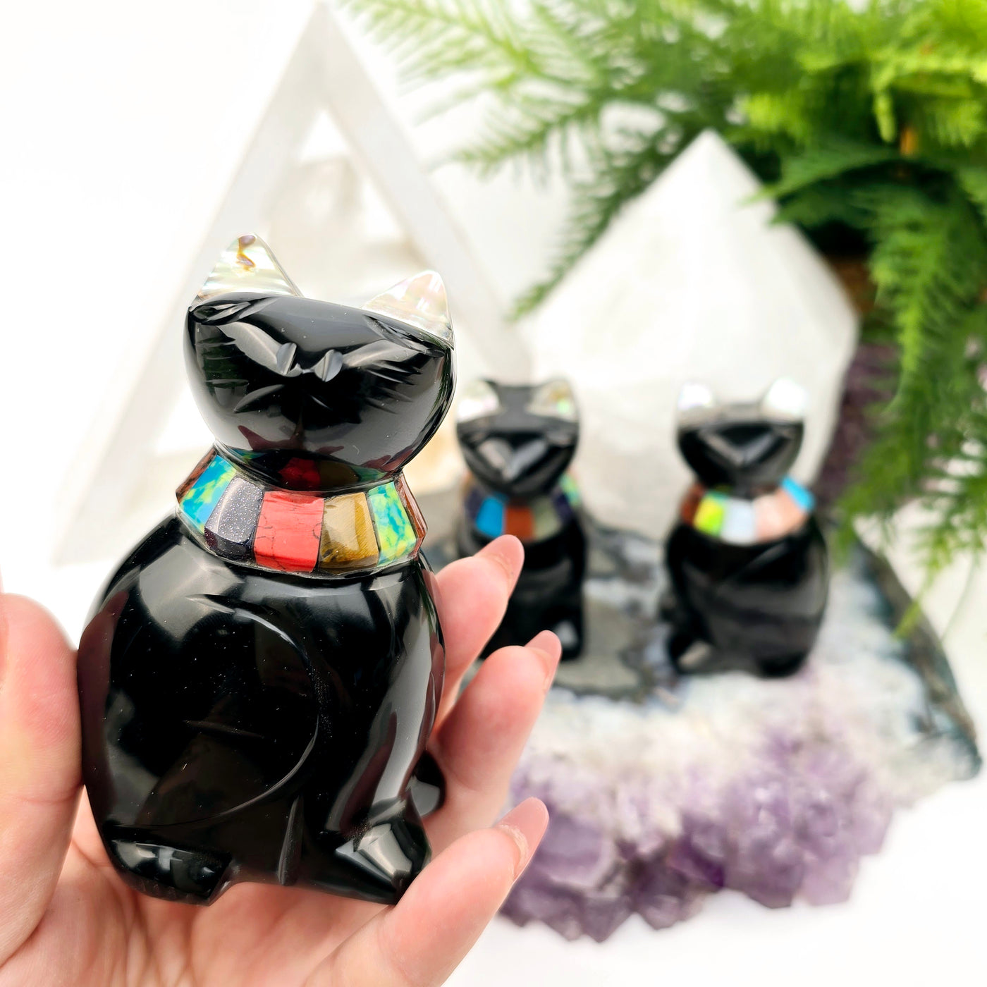  Black Onyx Crystal Cat with Shell and Gemstone Inlays - You Choose - variant A in hand for size reference with other variants in the background on amethyst platter with props and plants