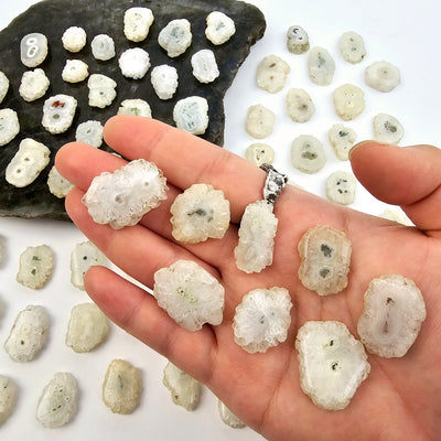 Crystal Stalactite Drilled Beads in hand for size reference with other stalactite beads in the background on stone platter and paper