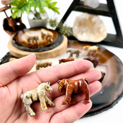 Soapstone Horse Carving from Peru - You Choose Color, both variants in hand for size reference with others in the background on stone platters with plants and props