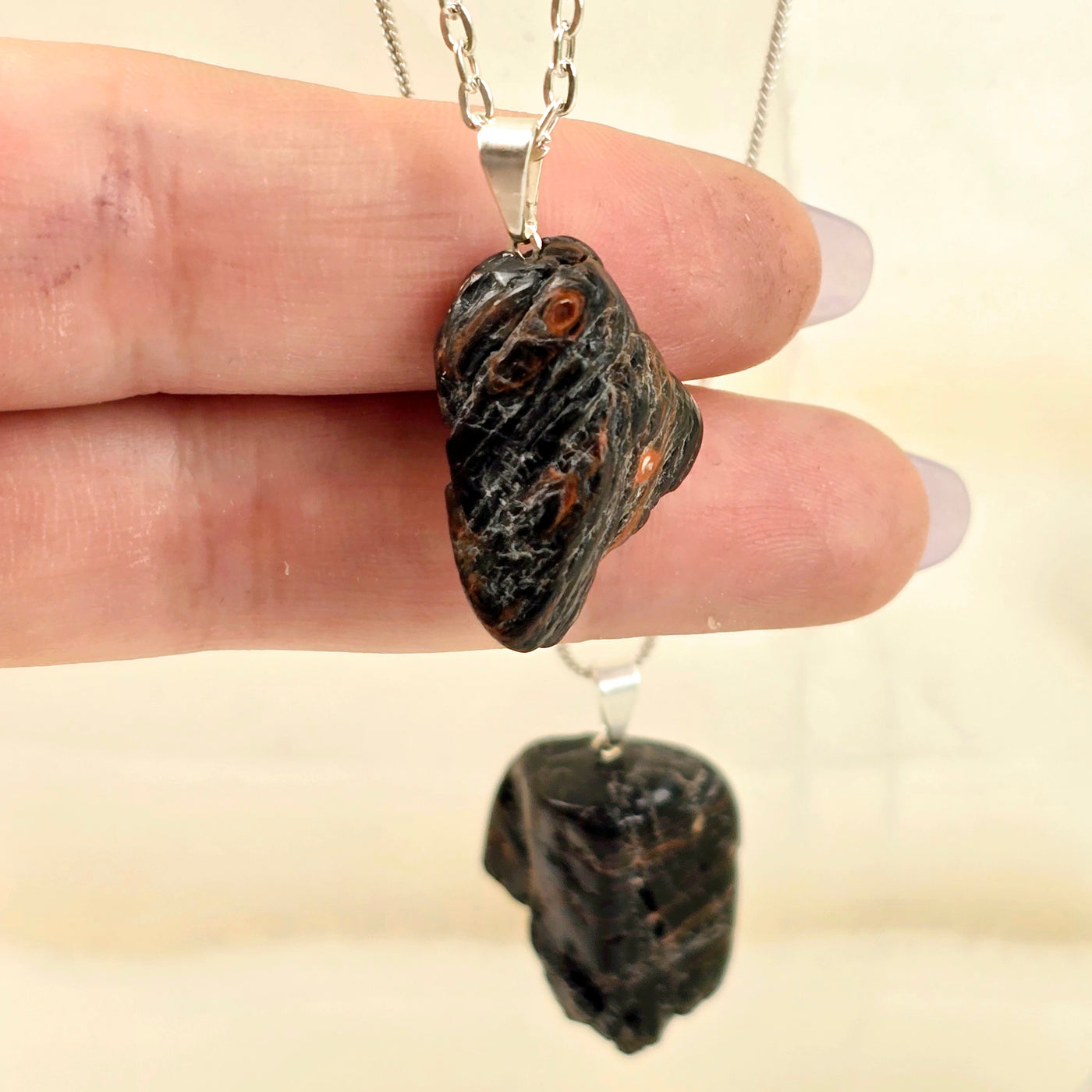 Black Tourmaline with Hematite Crystal Pendant with two fingers behind for size reference with another pendant on chain in the background