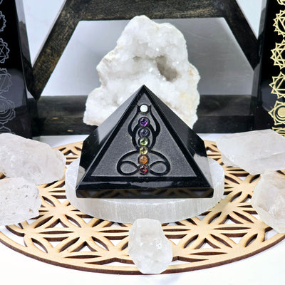 Black Obsidian Pyramid with Seven Chakra Crystal Accents - on selenite coaster on flower of life wood grid with crystals and props in the background