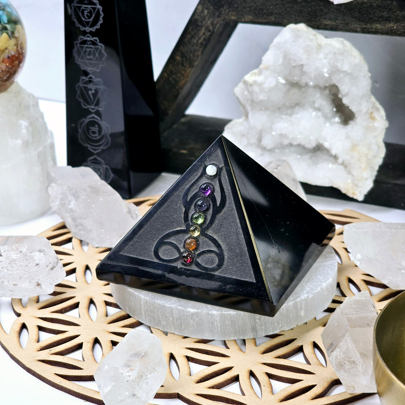 Black Obsidian Pyramid with Seven Chakra Crystal Accents side view with selenite coaster on wooden flower of life grid with crystals and props in the background