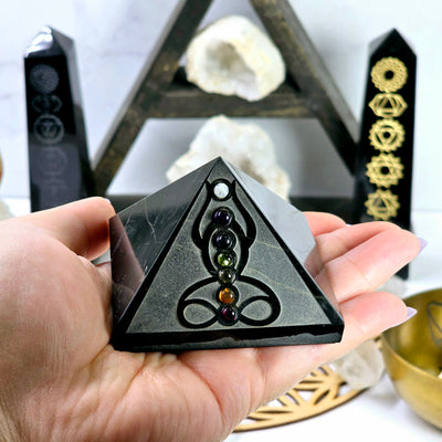 Black Obsidian Pyramid with Seven Chakra Crystal Accents in hand for size reference with props in the background