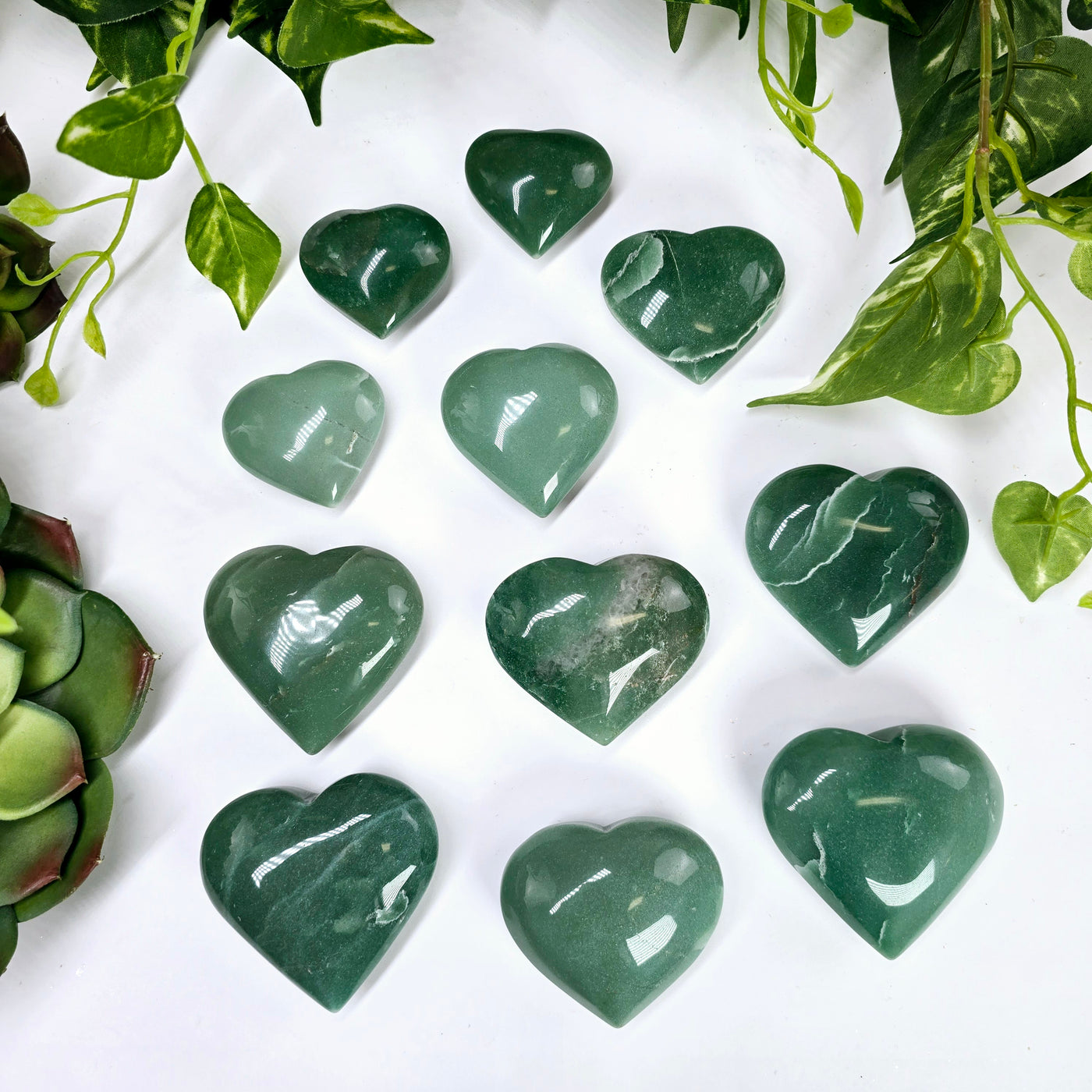 Green Aventurine Crystal Heart - By Weight - eleven hearts of all three variants with plants in the background