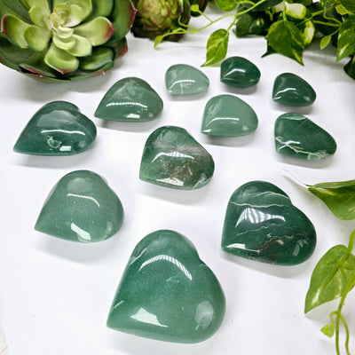 Green Aventurine Crystal Heart - By Weight - eleven hearts of all three variants side view with plants in the background