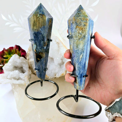 Blue Kyanite Crystal Wand on Stand - You Choose #2 variant 2 in hand for size reference with other variant on stone platter with props and plants in the background