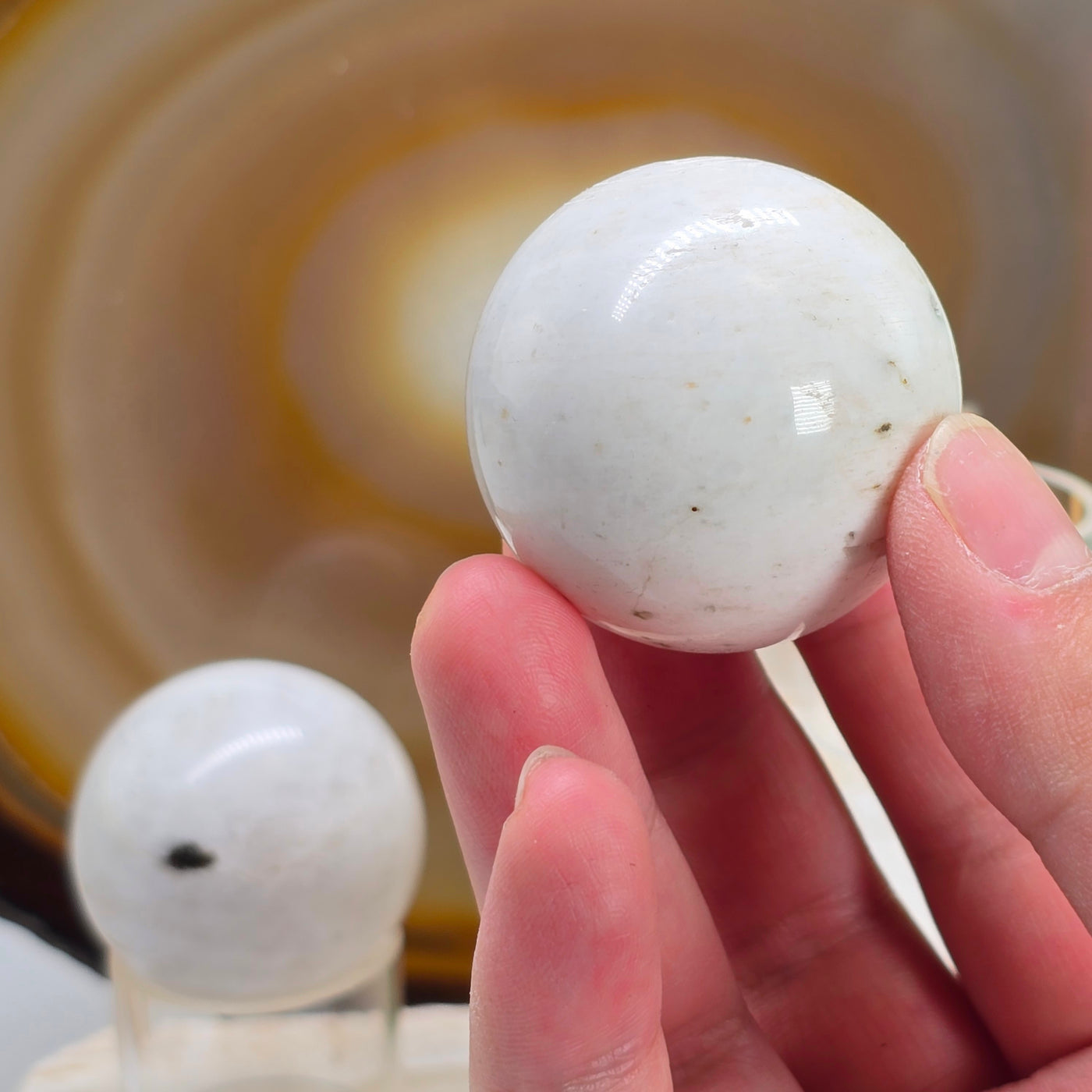 Scolecite Crystal Sphere - You Choose variant B in hand for size reference with other variant in the background with natural agate slice