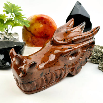 Mahogany Obsidian Crystal Dragon Head Carving 3/4 angle with props and plants in the background