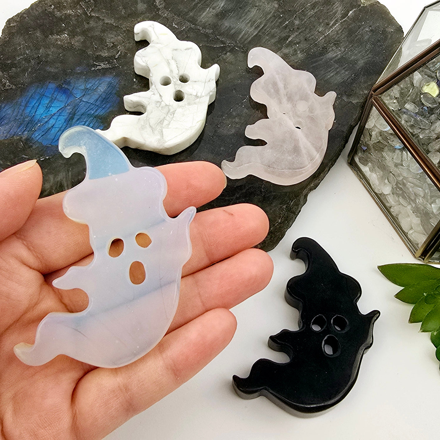 Crystal Ghost with Hat Carving - Halloween Decor - You Choose Stone - Opalite variant in hand with other variants on stone platter and white surface with props and plants in the background