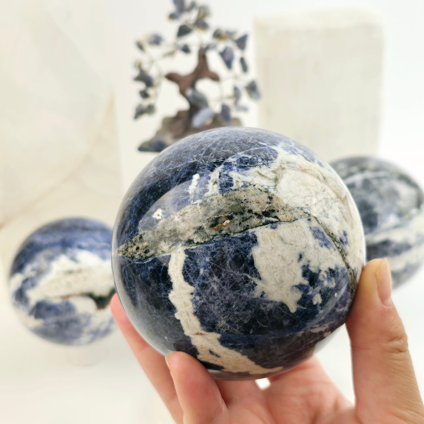 Sodalite Crystal Sphere - You Choose - variant 2 in hand for size reference with other variants in background with props