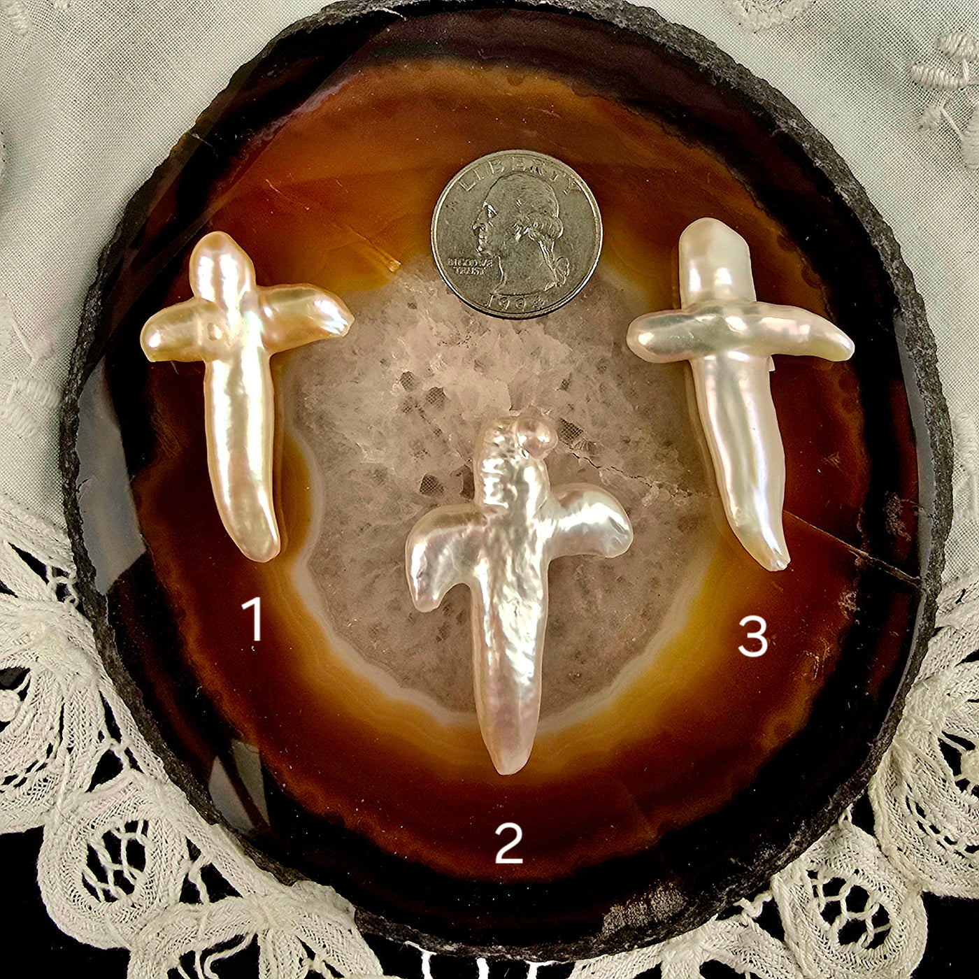 Cross Shaped Freshwater Pearl - Undrilled - You Choose variants 1, 2, and 3 labeled with quarter for size reference on natural agate slice over a white doily on black acrylic background