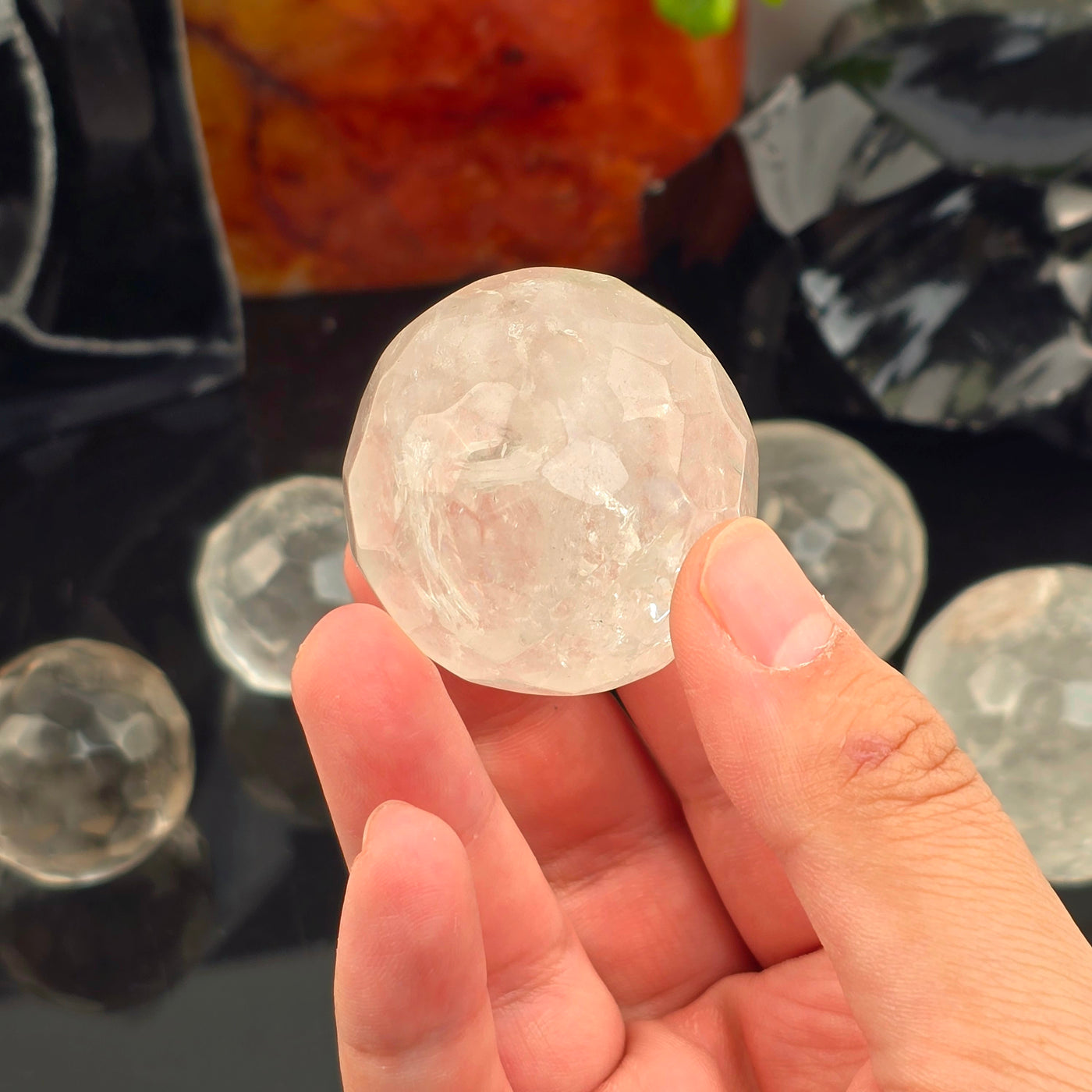 Crystal Quartz Round Faceted Sphere - You Choose - one variant in hand with other variants in the background on black acrylic with props