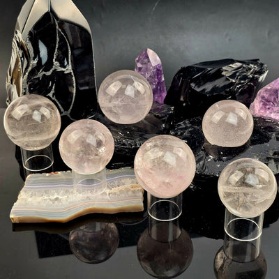 Rose de France Amethyst Crystal Sphere - You Choose all variants on sphere stands on black acrylic with black obsidian sphere holders and agate platter with amethyst points in the background