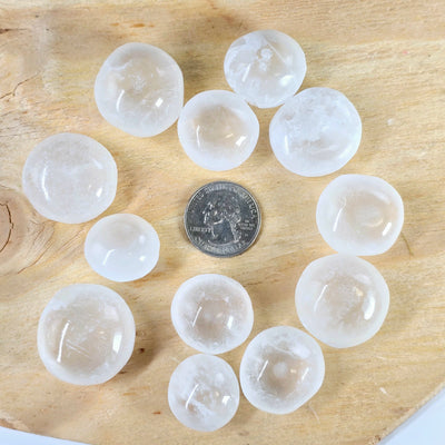 Optical Selenite Crystal Tumbled Stone - By the Piece - several stones with quarter for size reference on wooden platter