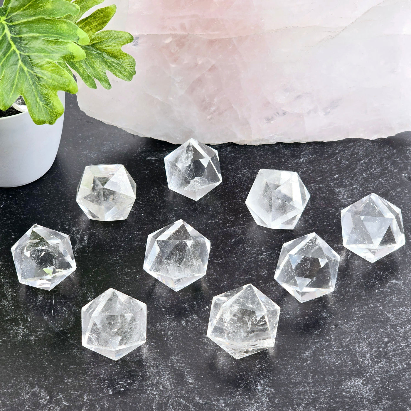 Crystal Quartz Small Icosahedron - nine shown on dark table with props and plants in the background