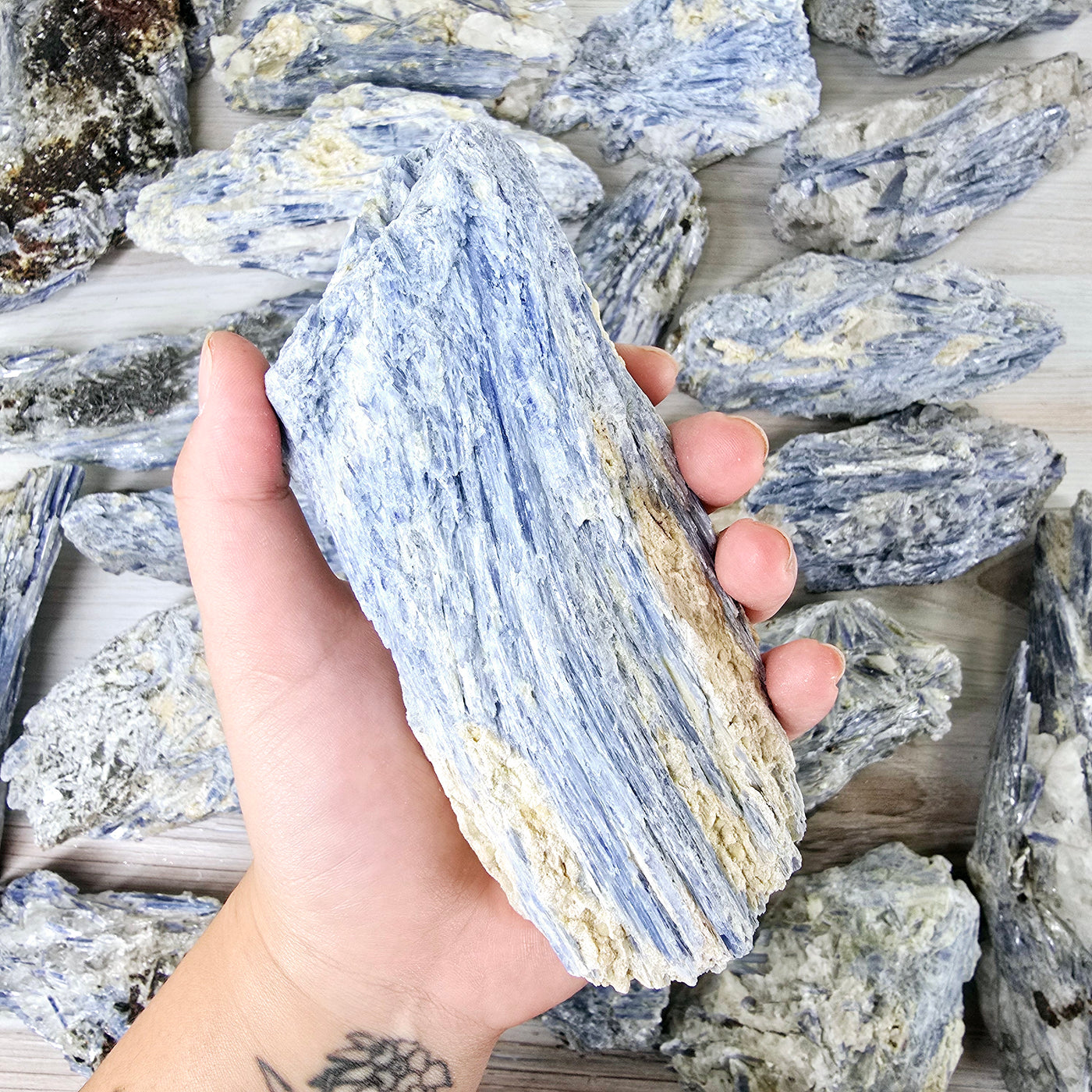  Blue Kyanite - Rough Crystal on Matrix - YOU CHOOSE #3 - variant 1 in hand for size reference with other variants in the background on wood surface