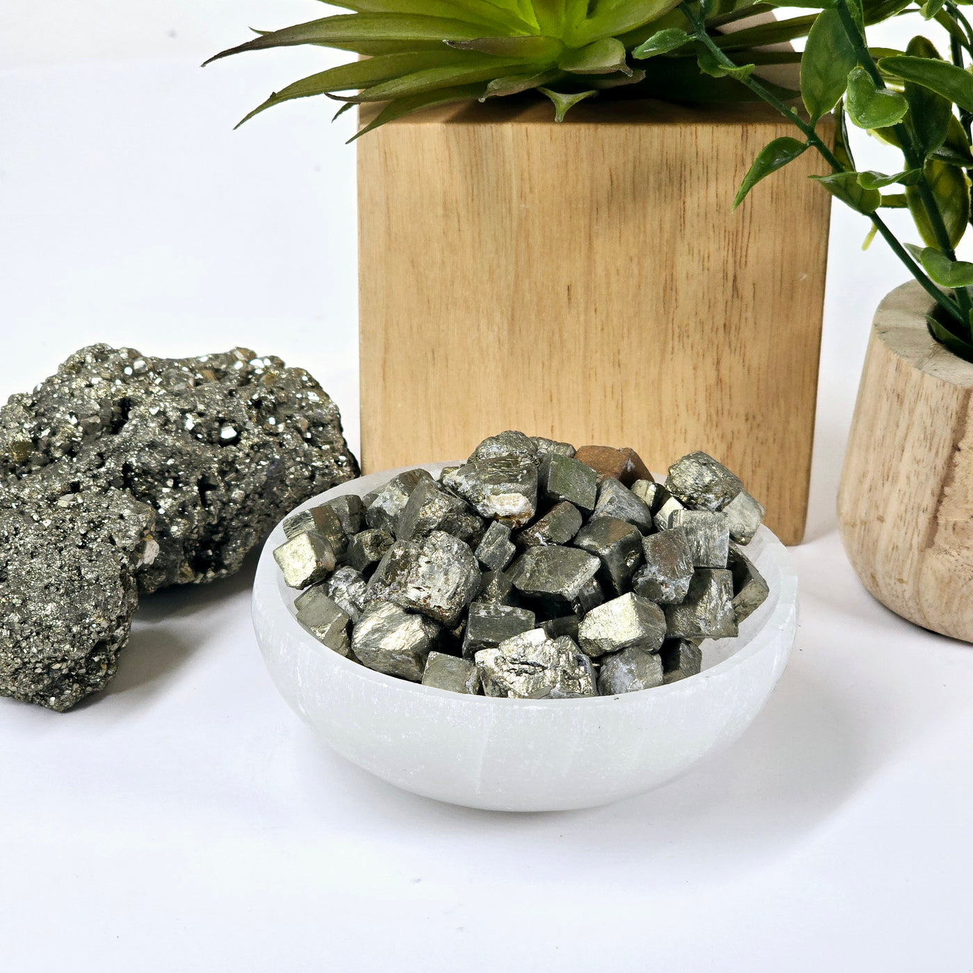 Pyrite Crystal Cubes - By the Pound in white bowl with props and plants in the background