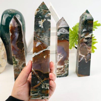 Ocean Jasper Polished Crystal Tower - You Choose #4 - variant 2 in hand for size reference with other variants in the background with props and plants