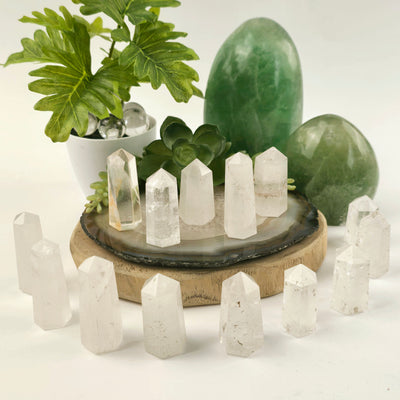 Crystal Quartz Small Obelisk Point multiple arranged in aesthetic way on stone and wood platter with plants and props in the background