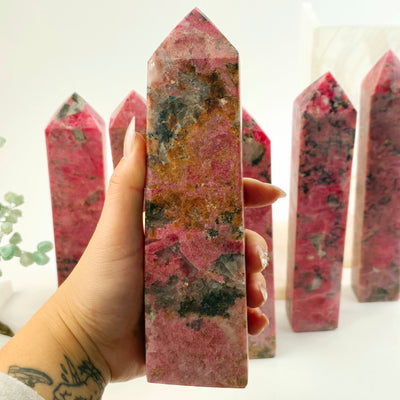 Rhodonite Polished Crystal Tower - You Choose #2 variant 1 in hand for size reference with other variants in the background with props