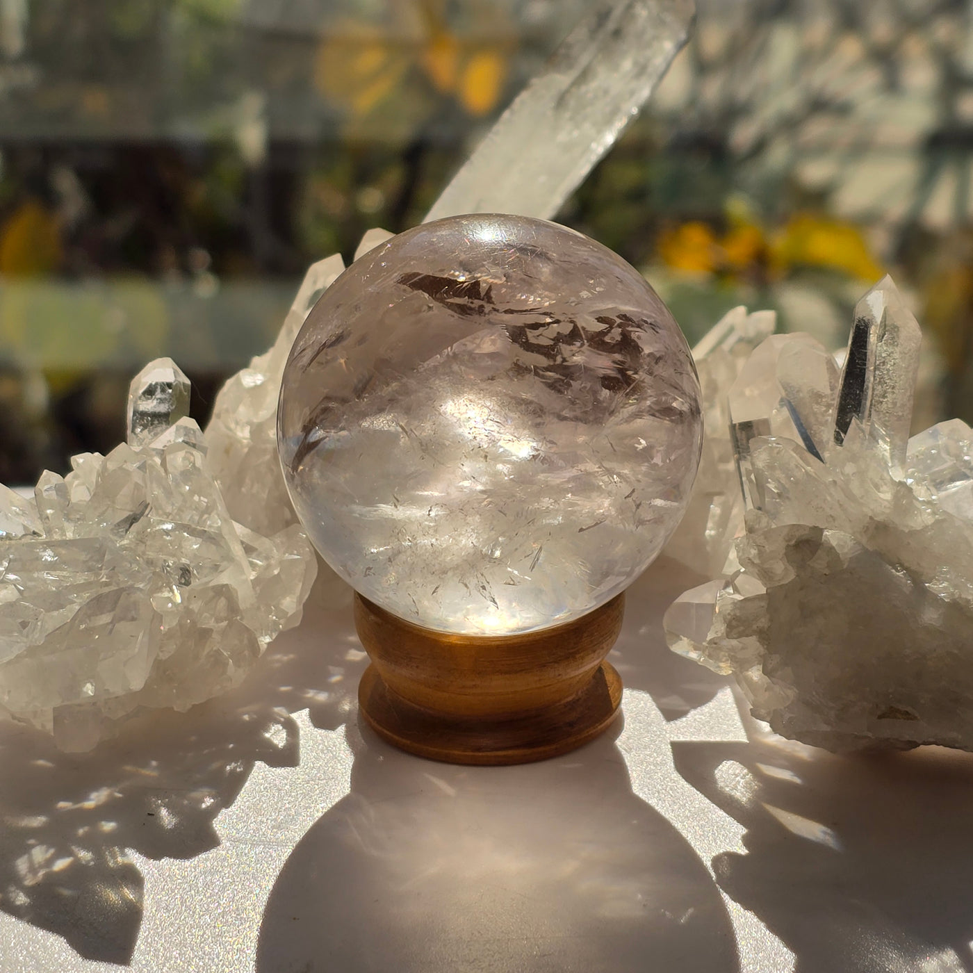 Rose de France Amethyst Crystal Sphere - One of a Kind surrounded by high quality quartz backlit by sunlight with plants in the background