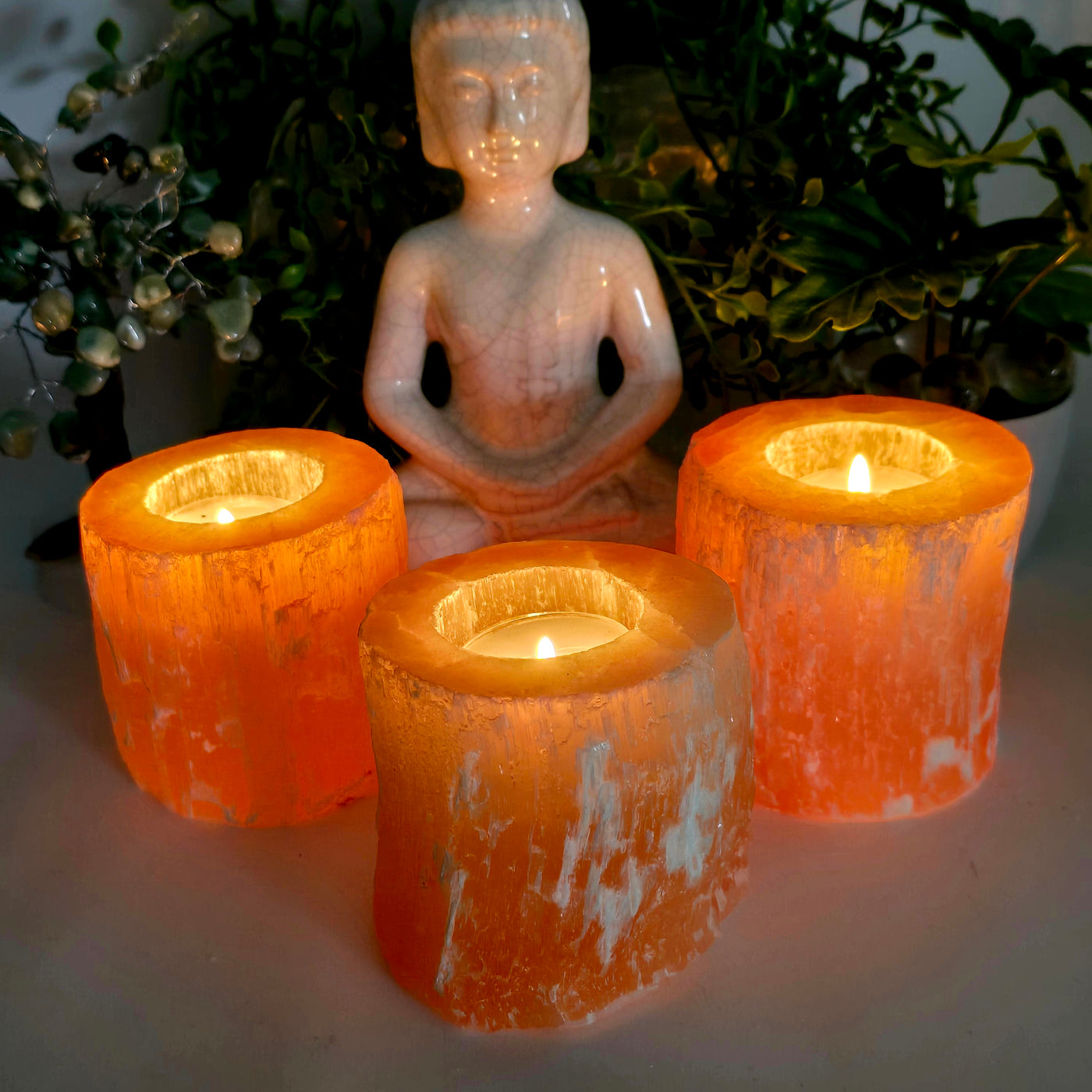 Orange Selenite Crystal Candle Holder with candles lit in dim lighting with props and plants in the background