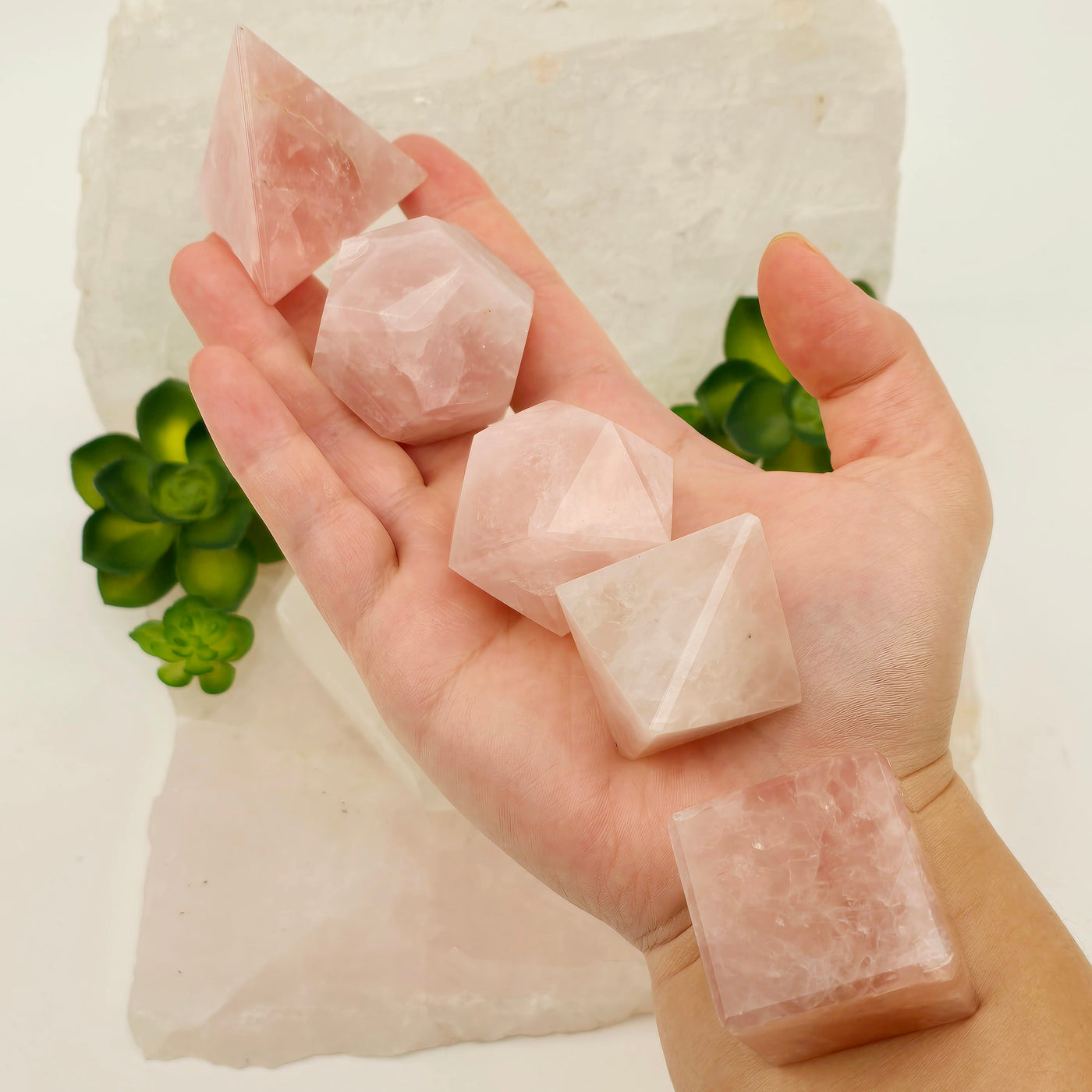 Rose Quartz Crystal Set of 5 Platonic Solids - Sacred Geometry all in hand for size reference with props and plants in the background